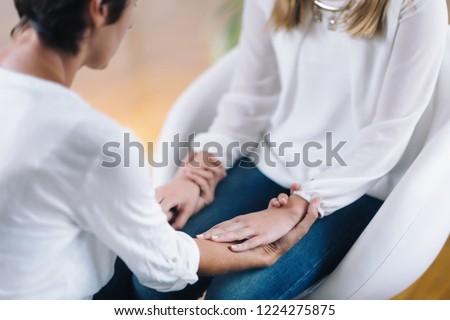 Female Theta healing therapist performing alternative therapy treatment with young woman patient. Therapist holding hands and transfer energy. Wearing white clothes. Royalty-Free Stock Photo #1224275875