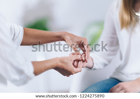 Female Theta healing therapist performing alternative therapy treatment with young woman patient. Therapist doing applied and muscle testing by holding hands. Wearing white clothes.  Royalty-Free Stock Photo #1224275890