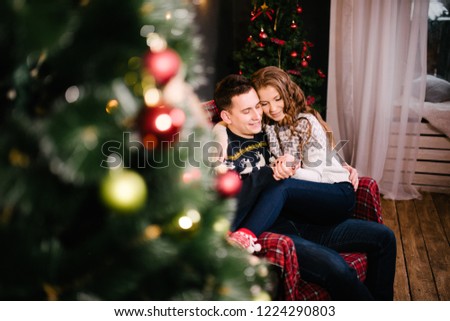 The guy and the girl in woolen sweaters and socks are sitting by the Christmas tree