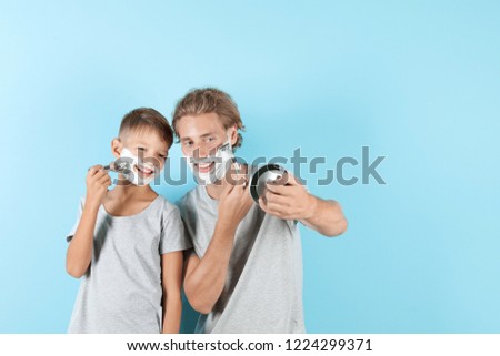 Father and son shaving together on color background, space for text
