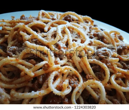 Spaghetti Bolognese with minced beef, onion, chopped tomato, garlic, olive oil, stock cube, tomato puree and Italian herb. Traditional Italian food in white plate on black background. 