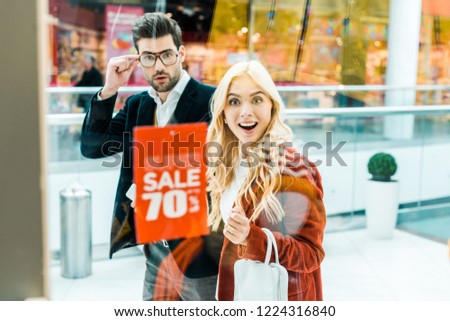 surprised couple looking at super sale with 70 percents discount in shopping center