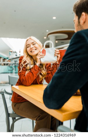 happy attractive woman showing bag with sale tag to boyfriend in shopping mall