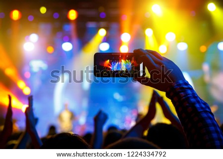 Man in the crowd at a concert make video recordings and pics on a smartphone of published in social media