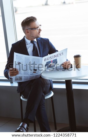 adult businessman reading newspaper and looking at window at airport
