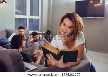 A girl student reads a book against the background of friends.