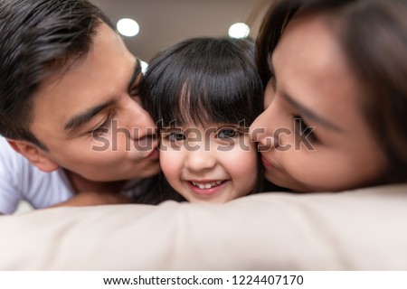 Asian Parents kissing their little daughter on both cheeks.