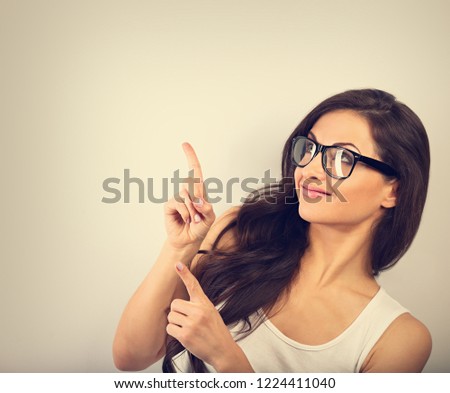 Beautiful excited smiling casual woman in eye glasses pointing the finger up and smiling on empty copy space background. Toned closeup portrait