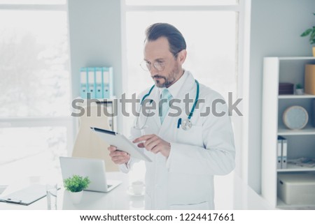 Confident concentrated focused calm attractive pharmacist surgeon intern practitioner therapist man stand inside light white hospital hold gadget in hands Royalty-Free Stock Photo #1224417661