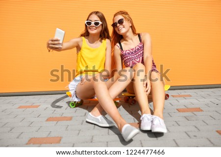 friendship, leisure and technology concept - happy teenage girls or friends with short skateboards taking selfie by smartphone on city street in summer