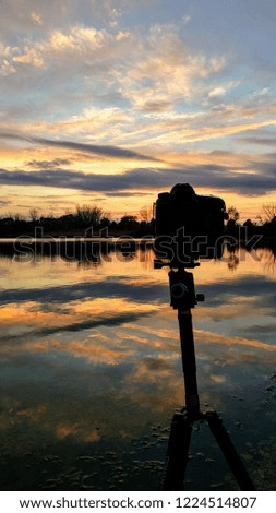 A camera taking a picture of a beautiful sky with the orange sunset reflecting onto the water.