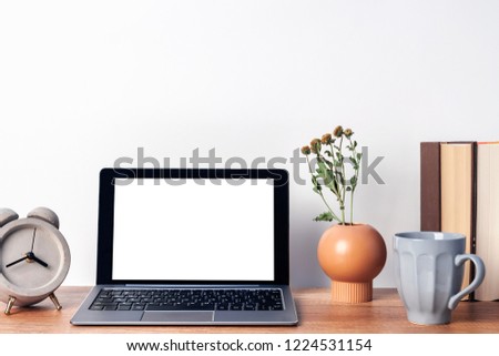 Wooden desk with an open laptop mockup, a vase with dried flowers, a concrete gray clock, a mug of coffee and books on the background of a white wall copy space