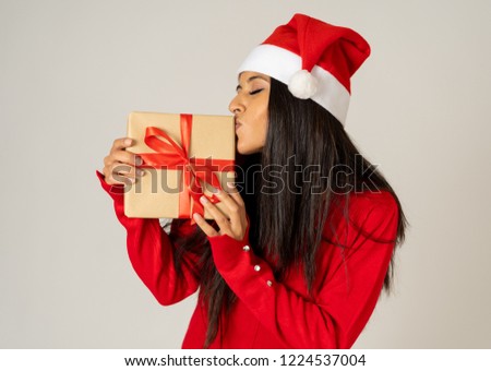 Young happy woman in red sweater and hat looking excited showing Christmas gift recycled paper isolated on grey background in shopping Christmas holidays shopping happiness celebration concept.
