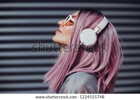 Beautiful young girl with purple pink hair listening to music on headphones, street style, outdoor portrait, hipster girl, music, mp3, Bali, beauty woman, sunglasses, orange color, concept Royalty-Free Stock Photo #1224555748