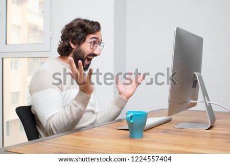 young bearded crazy freelancer working with his computer in the office and expressing a concept