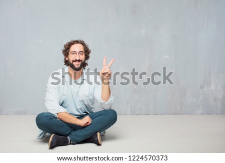 young crazy man sitting. smiling and looking satisfied and happy, counting number two with fingers.