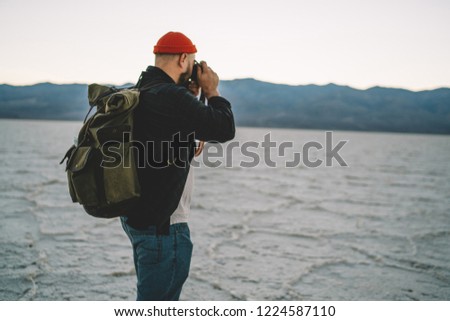Back view of male with backpack taking picture of beautiful nature and landscape during trip to Badwater basin, hipster guy fond of photography making image during expedition in desert lands