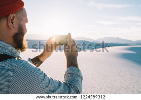 Cropped image of guy wanderlust making photo of desert dunes landscape on smartphone camera during trip,close up view of male traveler shooting video on White sands via app on telephone for blogging