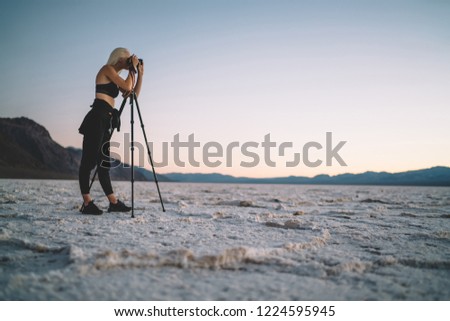 Skilled female photographer standing with modern camera and tripod for taking photos of evening scenery of landscape and sunset,woman making pictures of dry arid lands of death valley during trip
