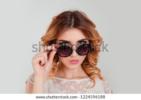 Head shot serious angry bitchy woman wife holding sunglasses down skeptically looking at you isolated light gray wall background, lace dress. Human face expression body language, attitude, perception