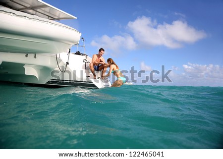 Young people swimming in the sea next to sailboat