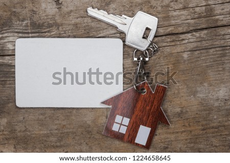 Silver key and blank business card on wooden background. Real estate concept. 