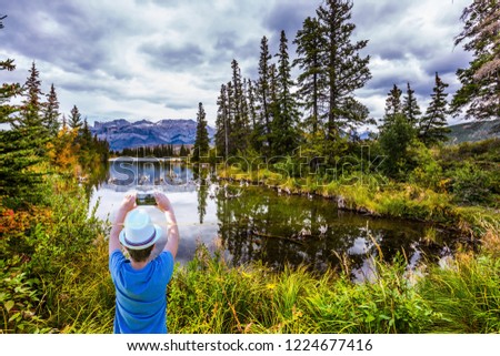 Boy in a white hat photographs a landscape cell phone. The lakes, firs and mountains of Canada. The valley along the Pocahontas road. Concept of active and photo-tourism