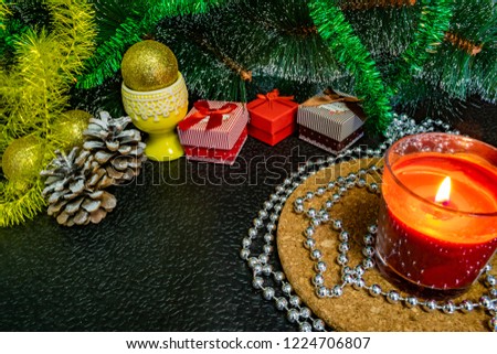 Festive Christmas composition with wax candles, gift boxes and silver beads. Decorations for new year's eve. On a dark background in warm light decorations, cones, stand and lights among the green pin