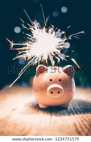 Piggy Bank with Sparkling Bengal Flamer on Wooden Table. Christmas and Happy New Year Festive Background with Bokeh Lights and Decorations. Royalty-Free Stock Photo #1224751579
