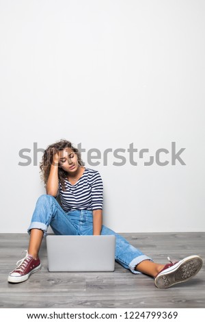 Sad  woman dressed in casual outfit, sits bare foot on wooden floor in empty room with laptop.