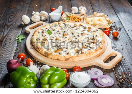 Big pizza with wild mushrooms and cheese on a round cutting board on a dark wooden background. Ingredients.