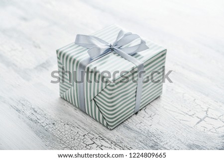 One striped  gift box with grey ribbon on white wooden background  closeup
