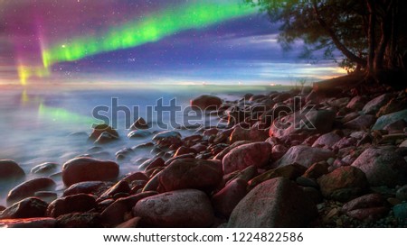 Intense northern lights (green, red Aurora borealis, Polar lights) over Baltic sea, Tallinn. sky reflection in water, stones, rocky beach. Beautiful landscape. Elements of this image furnished by NASA