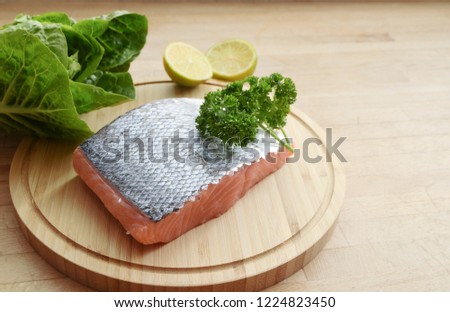 fresh salmon fillet with skin, lettuce and lemons on a wooden kitchen board, copy space, selected focus, narrow depth of field