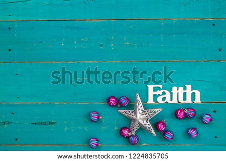 The word Faith hanging on antique rustic teal blue wooden background with colorful turquoise and pink Christmas ornaments and silver star;  religious holiday and spiritual wood sign with copy space