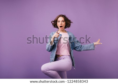 Shocked brown-eyes woman jumping on purple background. Joyful short-haired girl in jacket dancing. Royalty-Free Stock Photo #1224858343