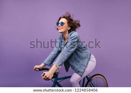 Dark-haired joyful lady chilling during photoshoot on bike. Winsome caucasian girl with wavy hair sitting on bicycle.