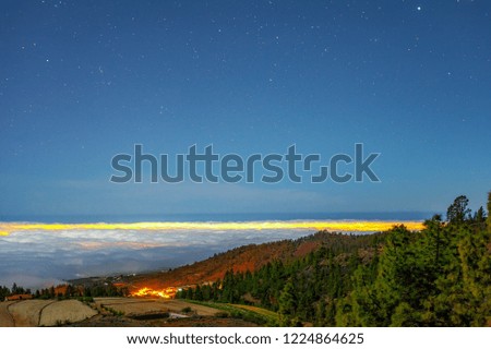 Night view on the city of Vilaflor above the clouds high from the mountains in alpine woods with lots of stars at background