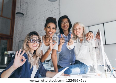 Team of young freelance specialists having fun in office and laughing. Attractive female web-developer using computer and posing for photo with international friends.