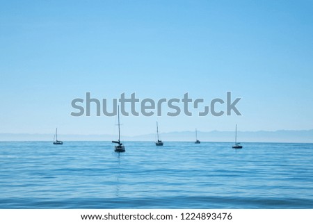Sailboats moored offshore in a sea bay, with a bright blue background and space for text on top