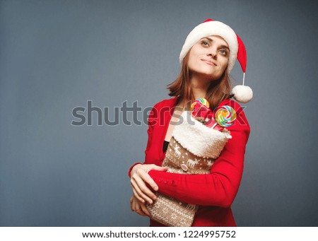 Young cheerful  girl in Santa's hat and with a Christmas sock with gifts, on a blue background. Celebration of new year and Christmas