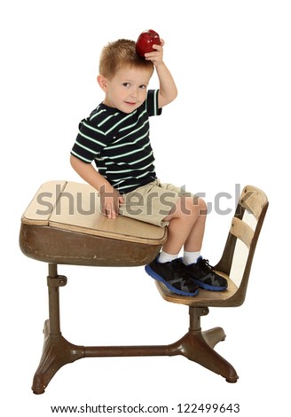 A school boy sits on a desk holding an apple on his head isolated on white Royalty-Free Stock Photo #122499643