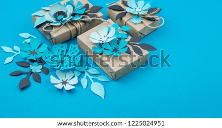 Gift box wrapped in craft paper blue background. Sakura flower made from paper origami. Present.