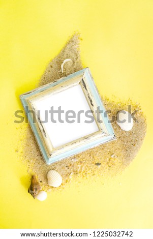 Empty photo frame with sea shells on sand over yellow paper. Travel, beach vacation concept. Text space.