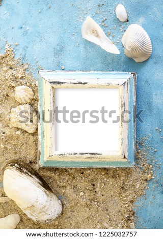 Empty photo frame with sea shells on sand over blue paper. Travel, beach vacation concept. Text space.