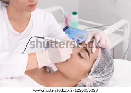 Young woman undergoing procedure of permanent eyebrow makeup in tattoo salon