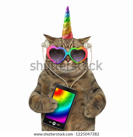 The unicorn cat in headphones is listening to music from a smartphone. White background.