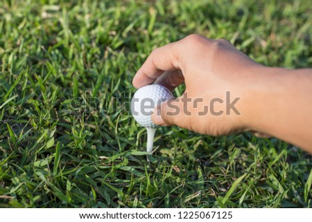 Hand with Golf ball on green background.