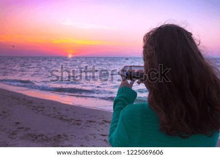 Girl takes pictures on the smartphone sunrise at the sea
