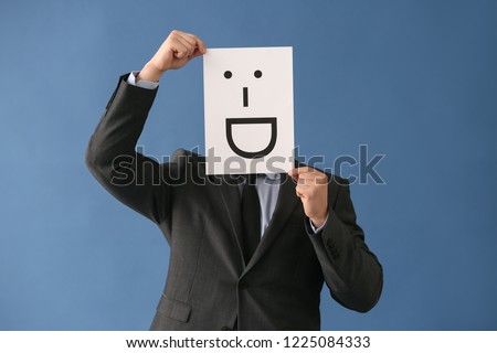 Businessman hiding face behind sheet of paper with drawn emoticon on color background